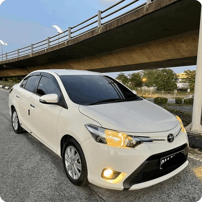 White Toyota sedan parked under a bridge with headlights on.