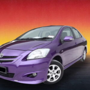 Purple compact sedan on a dark roadway with a warm city skyline glow.