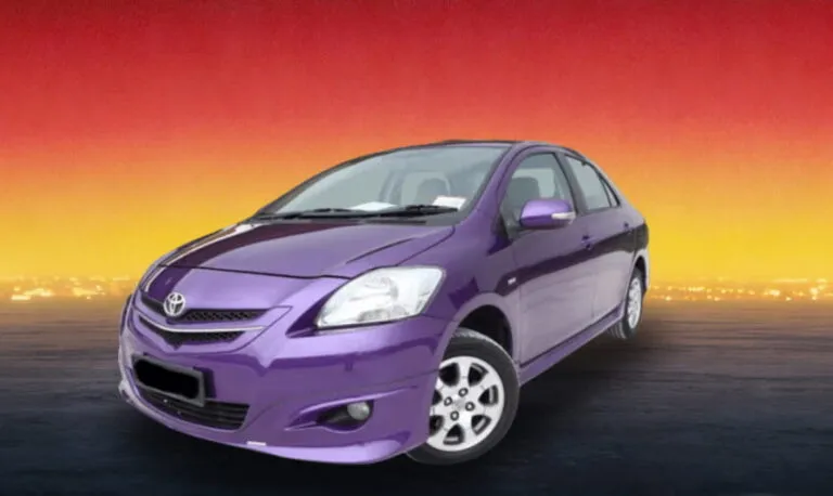 Purple compact sedan on a dark roadway with a warm city skyline glow.